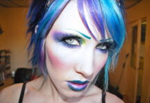 Hairstyles and Makeup Ideas For Vampires A woman displaying futuristic cyberpunk vampire makeup with purple and blue eyeshadow, a drawn-on teal eyebrow, metallic blue-rimmed ombre lips, and vibrant blue and purple hair.