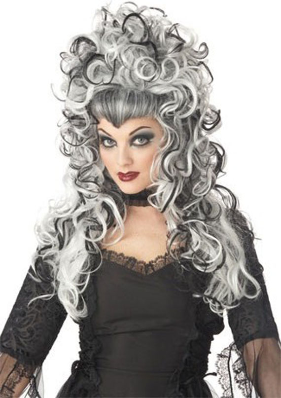 Woman in elaborate curly black and white wig wearing a gothic black lace dress. She has bold makeup and an intense, dramatic expression.