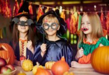 Halloween Holiday in Canada Three smiling children in witch and wizard costumes holding paper photo booth props like bat masks and vampire fangs at a decorated Halloween party table.