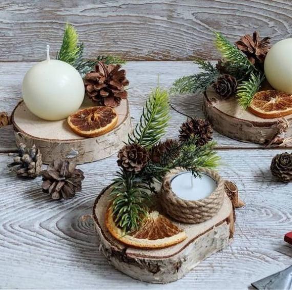 Eco-friendly Christmas candle holders on wooden slabs decorated with pinecones, evergreen branches, and dried oranges for a warm rustic holiday style.