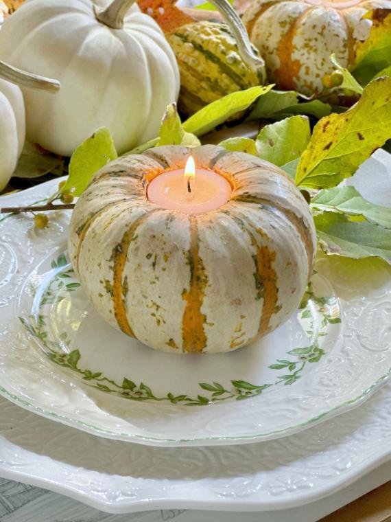 Mini striped pumpkin hollowed out and holding a lit pink tea light candle on a white plate with green botanical details.