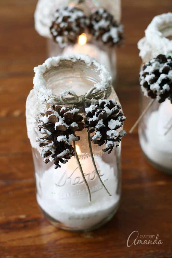 DIY Christmas candle jars decorated with pinecones and faux snow, creating a warm, rustic winter ambiance on a wooden table.