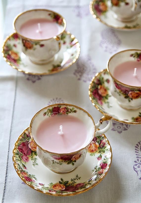 "Elegant Vintage Teacup Candle Holders with delicate floral patterns, each holding a soft pink candle. Arranged on a patterned light tablecloth, they create a charmingly Cozy Shabby Chic Ambiance for any setting."