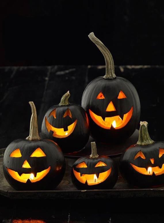 Black pumpkins with carved jack-o'-lantern faces glow warmly on a dark background, creating a spooky yet festive Halloween atmosphere.