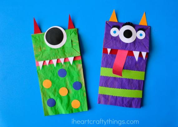 Two colorful, fun and silly monster puppets made from paper bags are displayed against a blue background. The green monster has spots, while the purple monster has stripes and a red tongue. Both have a single large eye and pointed teeth, with an overall playful and whimsical tone.