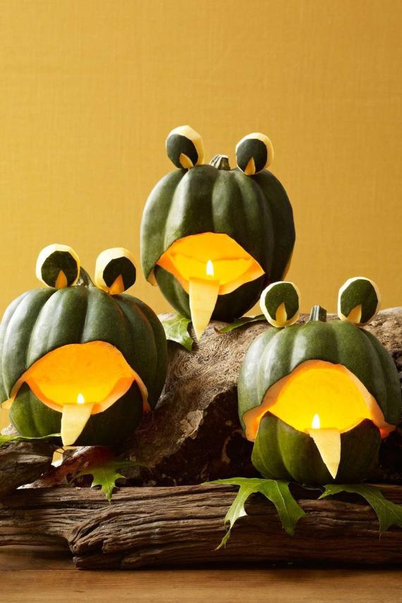 Three Easy Pumpkin Carving Designs of carved green pumpkins resembling frogs with open mouths and eyes sit on driftwood against a yellow background. Candles inside create a warm glow.