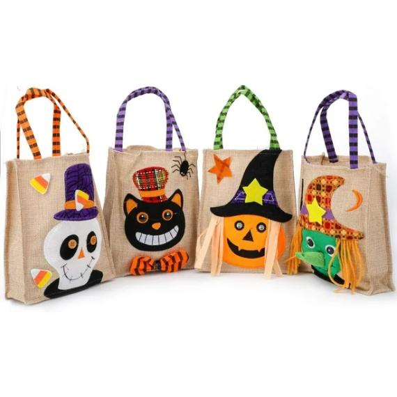 Four Halloween-themed burlap tote bags with colorful handles. Designs include a skull, black cat, pumpkin, and witch, decorated with hats and stars.