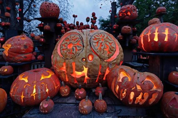 A collection of Creative Pumpkin Carving - jack-o'-lanterns in various sizes glow warmly at dusk. Their elaborate designs create a spooky, festive Halloween scene.