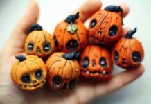 Easy Halloween Polymer Clay Ornament Projects Close-up of a hand holding seven small, Mini Pumpkin Ornaments with expressive, carved faces. The pumpkins convey a whimsical and eerie Halloween vibe.