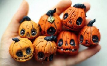 Easy Halloween Polymer Clay Ornament Projects Close-up of a hand holding seven small, Mini Pumpkin Ornaments with expressive, carved faces. The pumpkins convey a whimsical and eerie Halloween vibe.