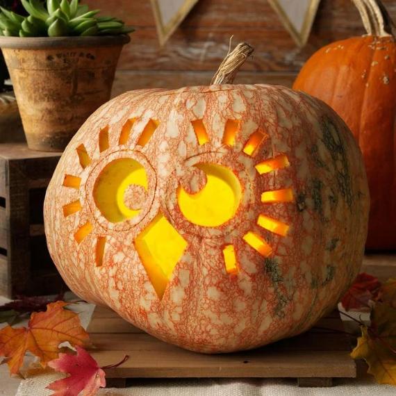 A Unique Jack-O’-Lantern Idea with an owl design, featuring spiral eyes and radiating lines, softly glows. Autumn leaves and another pumpkin are in the background.