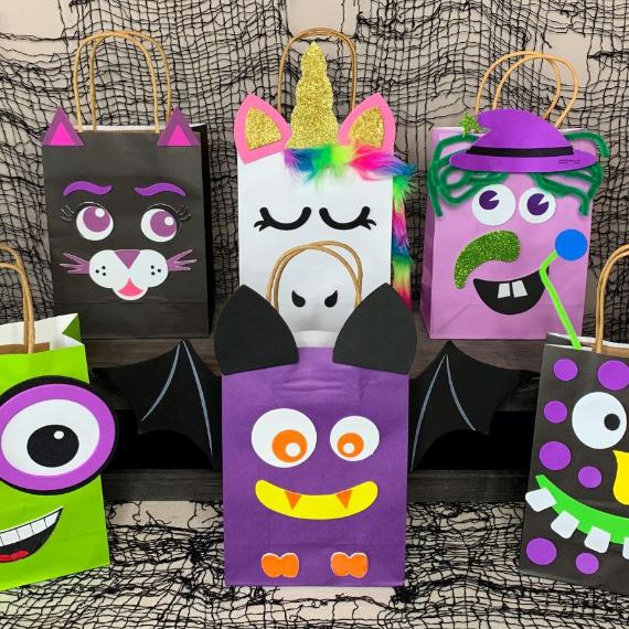 Colorful Halloween-themed gift bags with playful designs resembling a bat, unicorn, and monster, against a spooky netted backdrop. Fun and whimsical.