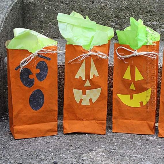 Three orange paper bags with jack-o'-lantern faces and green tissue paper protruding from the top. Each bag is tied with twine, set on steps.