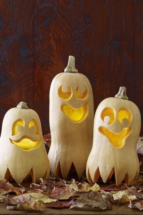 Three Easy Pumpkin Carving Designs in a ghost-shaped butternut squashes with smiling, carved faces glow warmly from within. Surrounded by dried leaves, the mood is playful and festive.