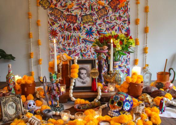 A detailed traditional Mexican Day of the Dead ofrenda altar for All Souls' Day featuring marigold garlands, sugar skulls, framed ancestor photos, lit candles, and colorful banners.