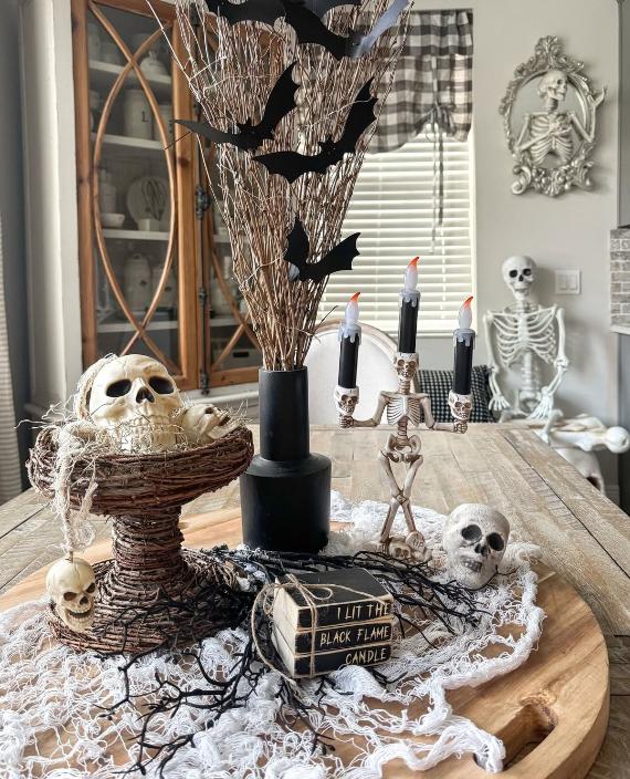 A Halloween table centerpiece featuring a skeleton candelabra with black flame candles, skulls, flying bats, and creepy cloth.
