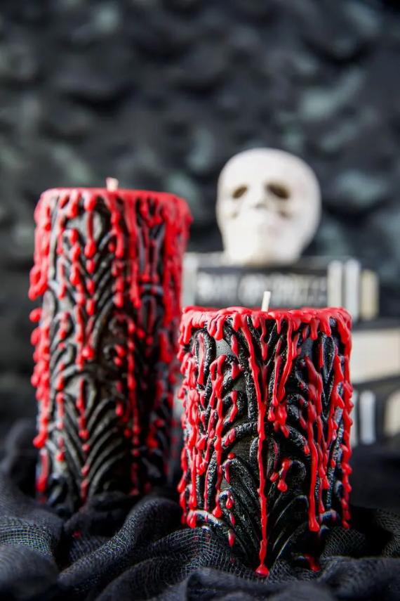 Two carved black damask pillar candles dripping with thick red wax in front of a white skull and books.