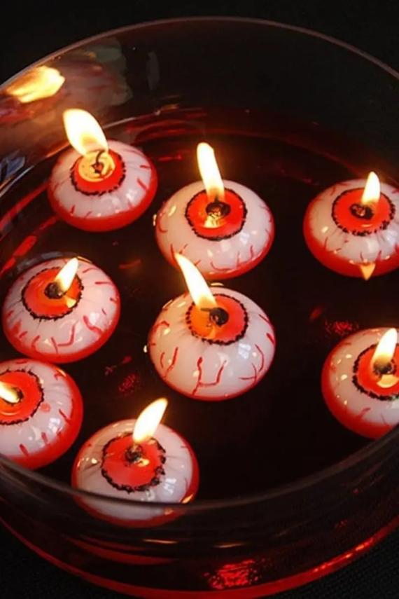 Eight lit floating eyeball candles with bloodshot red veins and orange irises floating in a bowl of dark red liquid.