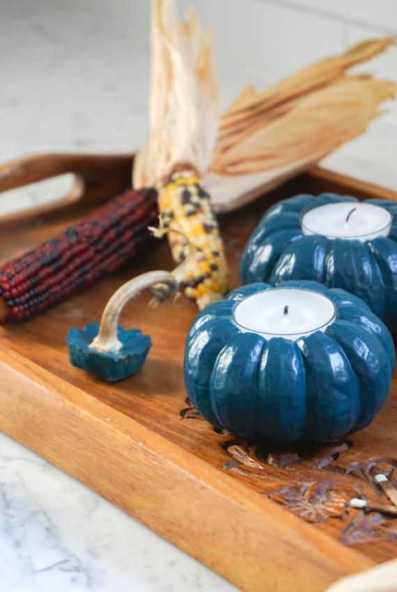 Teal pumpkin-shaped candles and dried corn on a wooden tray evoke a cozy autumn vibe. Warm Blue fall decorations, rustic tones create a welcoming, festive ambiance.
