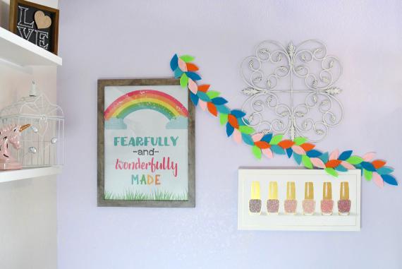 Unexpected fall color schemes of a pastel-themed wall features a framed rainbow print with "Fearfully and wonderfully made" text, colorful leaf garland, and framed nail polish display.