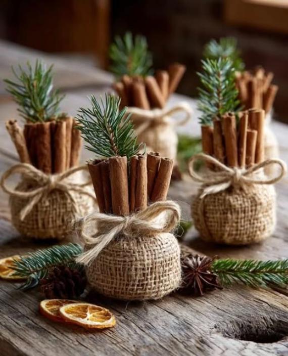Rustic bundles of cinnamon sticks tied with twine and evergreen sprigs sit on a wooden table, evoking a cozy, festive atmosphere with dried orange slices nearby.