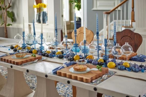 Elegant tablescape of Modern Blue Fall Decorating Ideas with Sapphire Blue Candles with blue and clear glass candleholders, yellow lemons, mini pumpkins, and pies on wooden trays. Bright, inviting atmosphere.