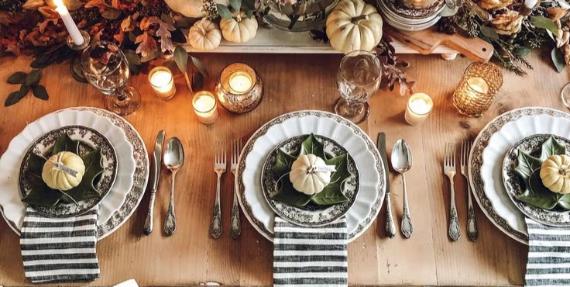 Autumn-themed dining table with plates, small pumpkins, candles, and a rustic centerpiece.