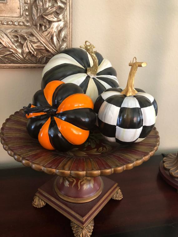 Three decorative pumpkins with black and white, and black and orange patterns on an ornate pedestal stand.