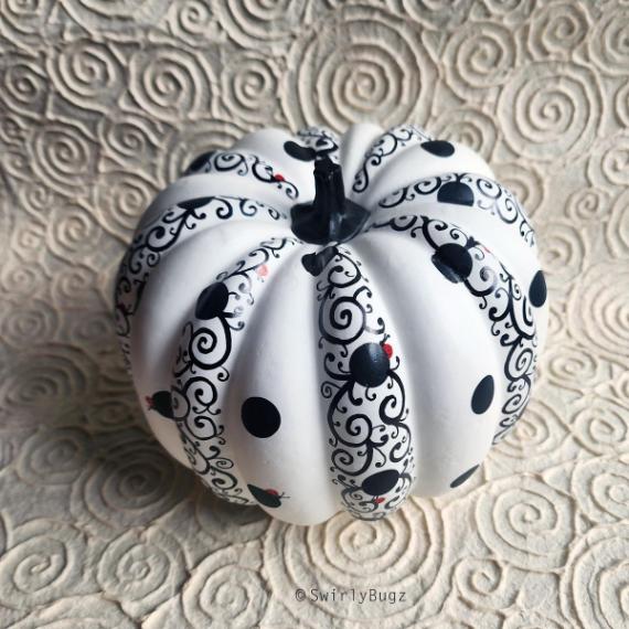 A white pumpkin with black swirls and dots, featuring red accents, on a textured swirling background.