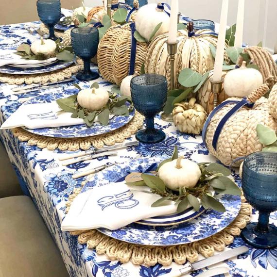 ElegantStunning-Fall-Tablescape-Decor-Ideas in blue floral tablecloth, wicker and white pumpkins as centerpiece. Blue glassware, white plates, and candles enhance the decor.