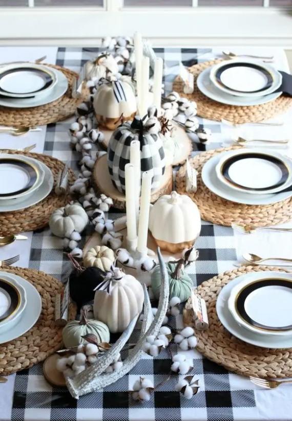 A fall-themed dining table set with woven placemats, decorative pumpkins, cotton branches, and candles.