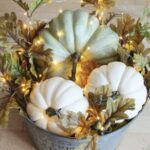 a-farmhouse-fall-centerpiece-of-a-bucket-with-fall-leaves-acorns-faux-pumpkins-and-lights-is-very-cozy