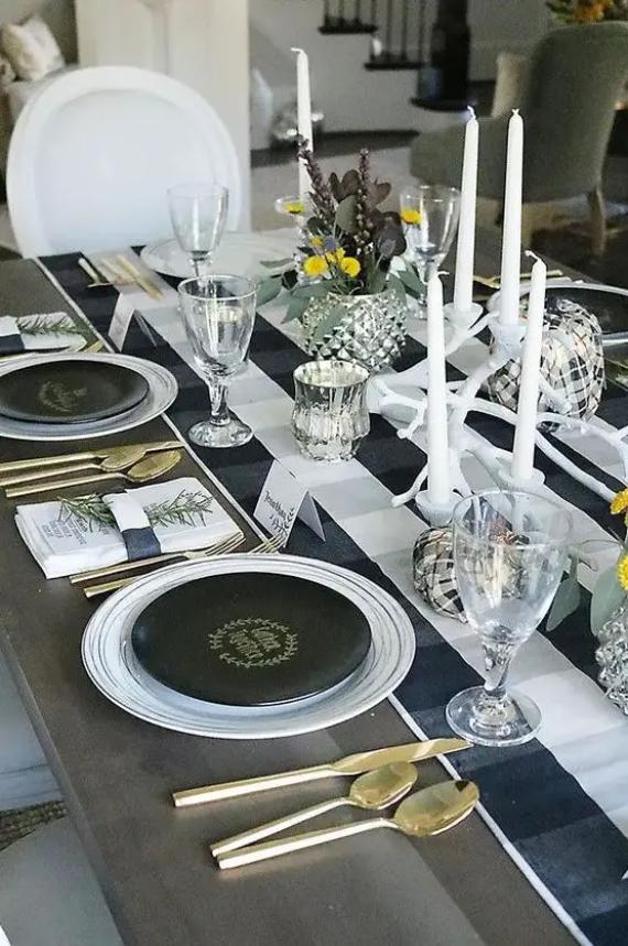 Elegantly set dining table with black and gold dinnerware, gold cutlery, and white candles.