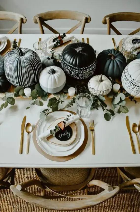 A dining table decorated with black and white painted pumpkins, green foliage, and gold cutlery.