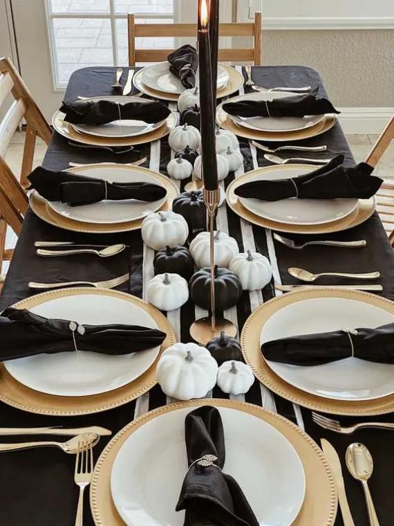 Elegant black and white Thanksgiving tablescape with a striped runner, gold chargers, gold candleholders, black candlesticks, small black and white pumpkins and black napkins.