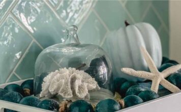 66 Inventive Seasonal Thanksgiving Décor Ideas With Blue A white tray holds teal ornaments, a starfish, a light blue pumpkin, and a glass dome with coral. Background features teal tiled walls, creating a coastal feel.