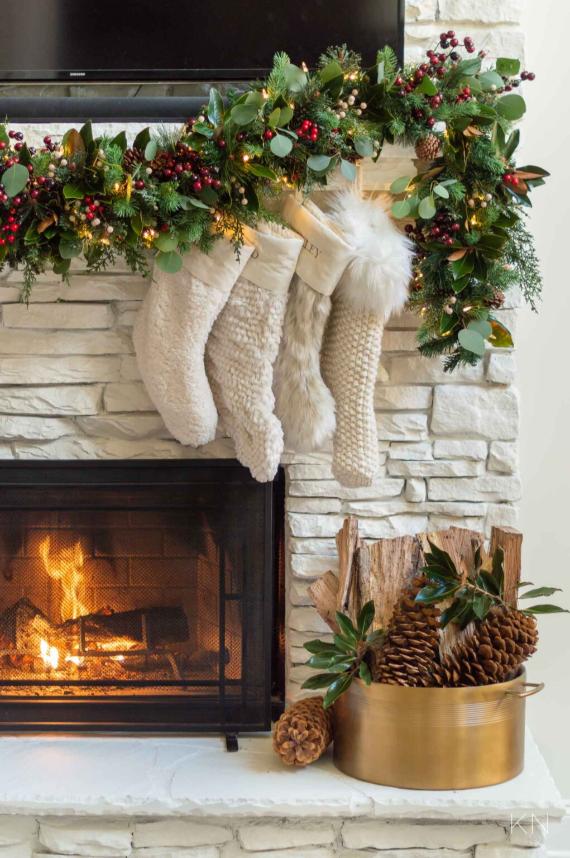 Festive scene with a cozy fireplace adorned with a lush garland of greenery and red berries. White stockings hang underneath, adding a warm, inviting holiday ambiance.
