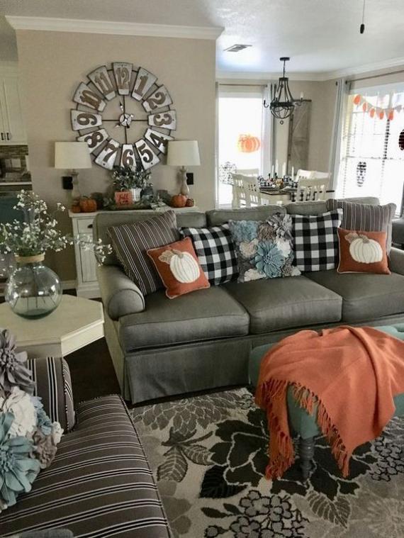 Living room with gray sofa, fall-themed cushions, large wall clock, and seasonal decorations.