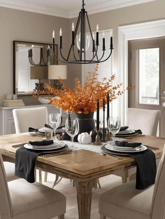 A dining table set with orange leaves centerpiece, black candles, and modern decor in a neutral-toned room.