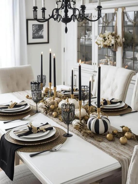 Elegant Thanksgiving tablescape in a white dining room with black and white table decor and gold accents, striped pumpkins, and plush white chairs, under a black chandelier.