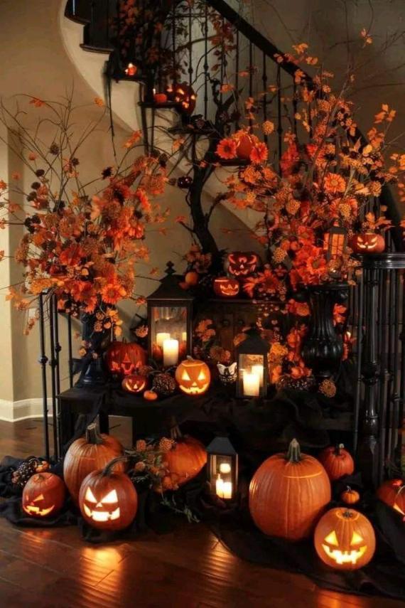 An elaborate indoor staircase display filled with glowing carved pumpkins, black metal lanterns with lit candles, and massive bursts of orange floral arrangements.