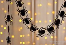 ‘Treat’ your Halloween Home with Festive Décor A festive black spider paper garland draped in front of a warm, blurry background of twinkling yellow fairy string lights.