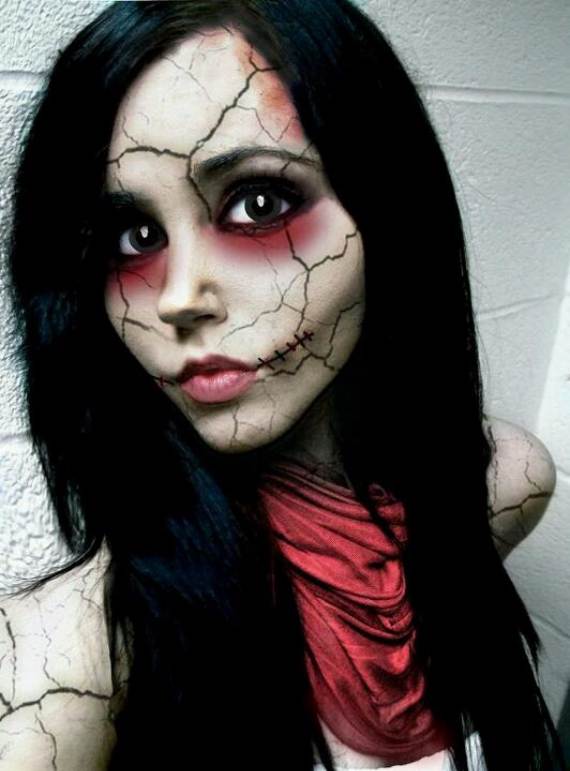 A Creepy Doll Makeup with long dark hair and Halloween makeup featuring cracked skin and stitched lips. Her eyes are wide and accentuated with dark shadows, creating an eerie effect. She wears a red scarf, conveying a haunting yet artistic vibe.