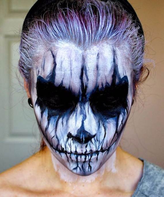 Ghostly white-out Skull Halloween Makeup person with detailed skull face paint featuring dramatic black and white streaks creating a haunting effect, set against a blurred indoor background.