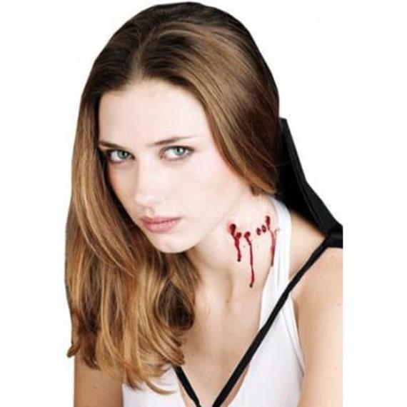 Easy and scary Halloween makeup of a woman with long brown hair looks directly at the camera. Red, realistic-looking fake blood drips down her neck, suggesting a vampire bite. Her expression is serious.