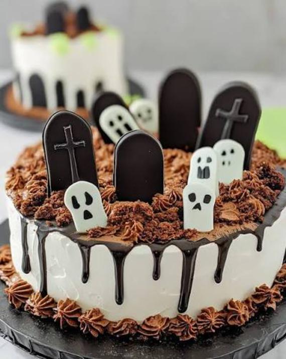 Halloween graveyard cake with white icing, dark chocolate drip, crushed cookie soil, chocolate tombstone cookies, and white fondant ghost cutouts.