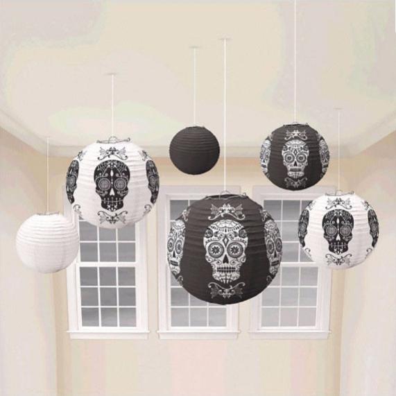 A cluster of black and white round paper lanterns printed with traditional Day of the Dead sugar skull designs hanging from a ceiling in front of windows.