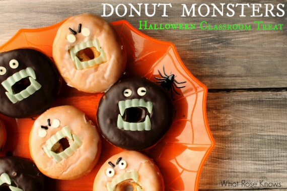 Glazed and chocolate-covered ring doughnuts decorated as monsters with plastic vampire fangs and small white candy eyes on an orange spiderweb platter.