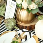 a-modern-rustic-Thanksgiving-tablescape-with-striped-and-chevron-linens-gold-chargers-and-cutlery-a-white-rose-arrangement-and-artichokes