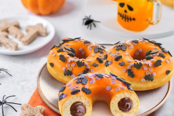 Assorted Halloween donuts with bright orange icing displayed on a white plate, showcasing seasonal designs.